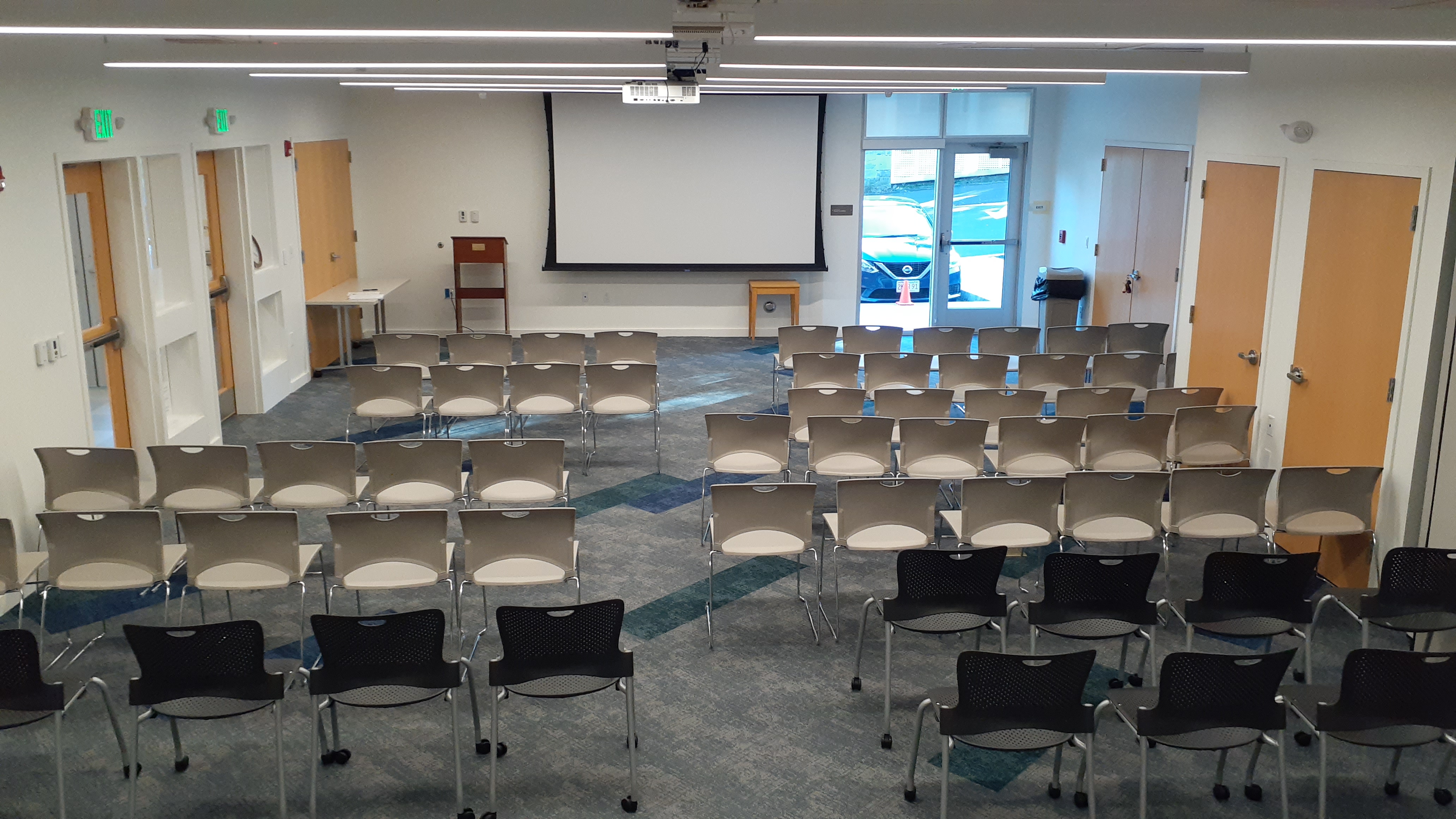 View of the Community Room from the back, with sveral chairs set up facing the projection screen on the front wall