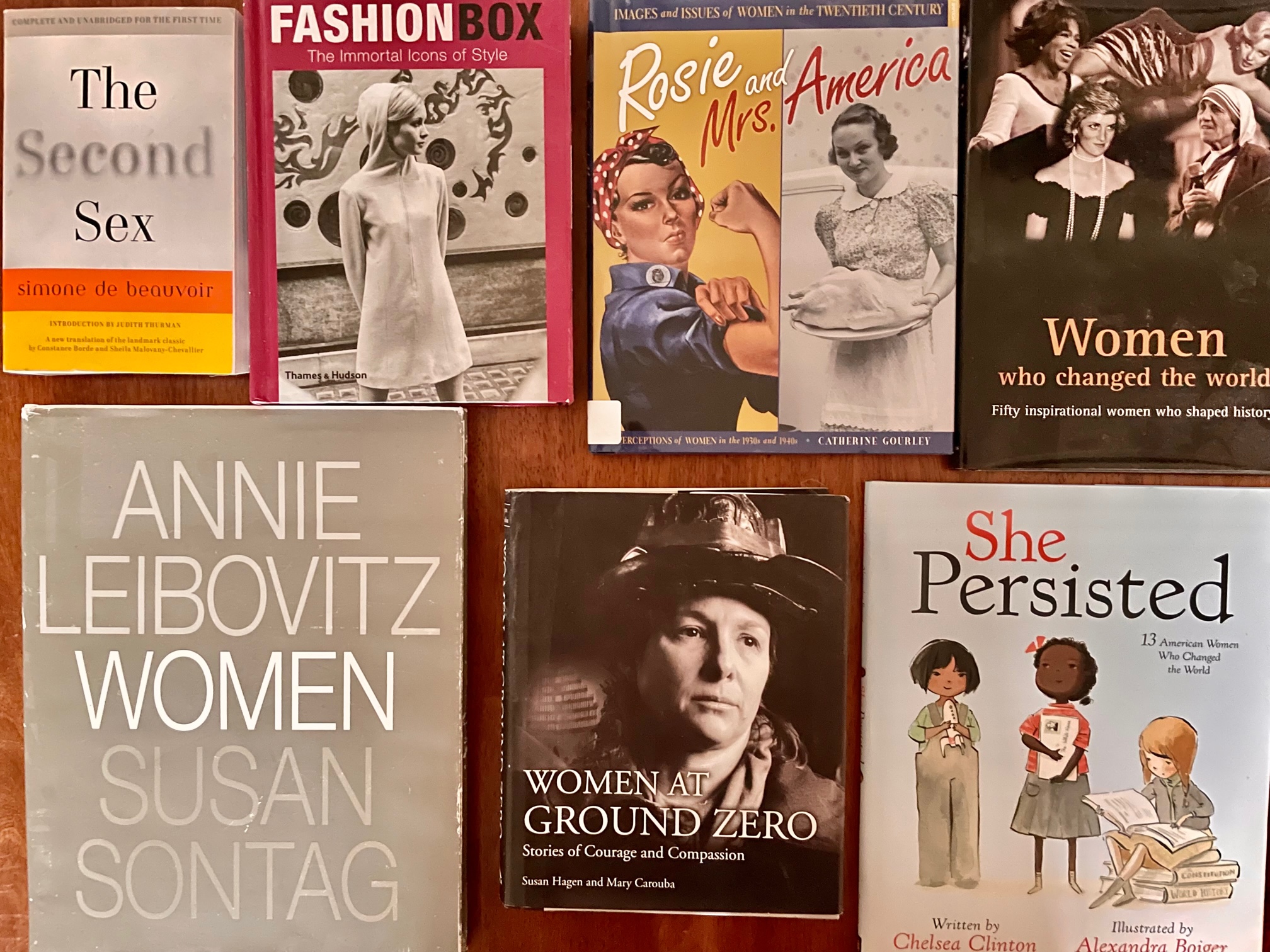 Photo of the book auction table. The books are: The Second Sex, Fashion Box: The Immortal Icons of Style, Rose and Mrs. America: Images and Issues of Women in the Twentieth Century, Women Who Changed the World, Women by Annie Leibovitz and Susan Sontag, Women at Ground Zero, and She Persisted.